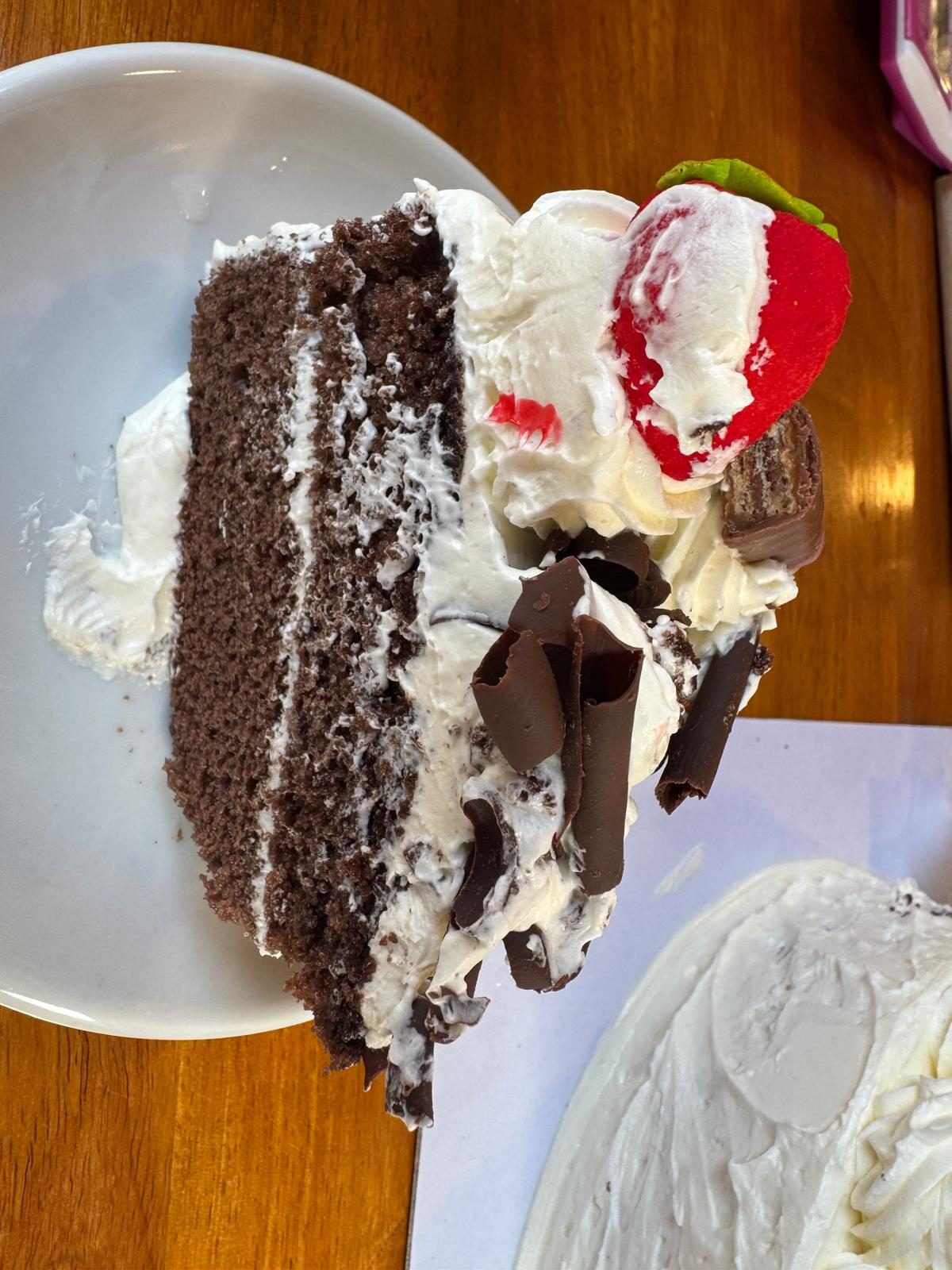 A slice of chocolate cake with cream, chocolate curls and a strawberry